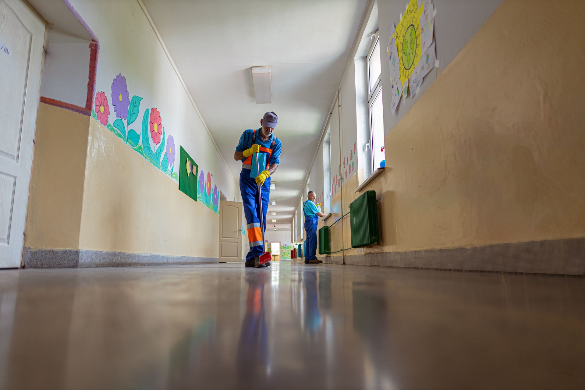 Two school janitors cleaning and disinfecting the empty school corridor